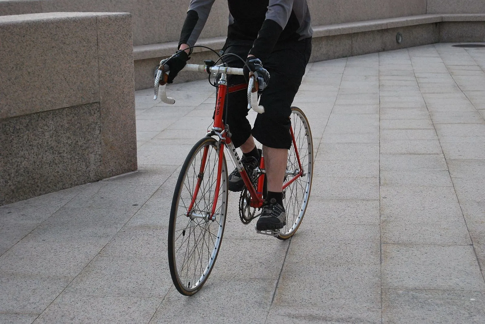Ciclista pedaleando en una bicicleta roja por una plaza de losas de granito