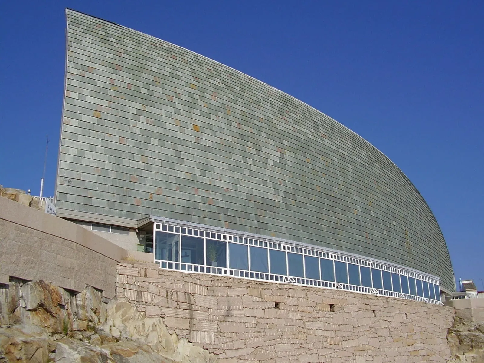 Fachada curva de pizarra de la Domus, la Casa del Hombre, sobre un muro de piedra en A Coruña