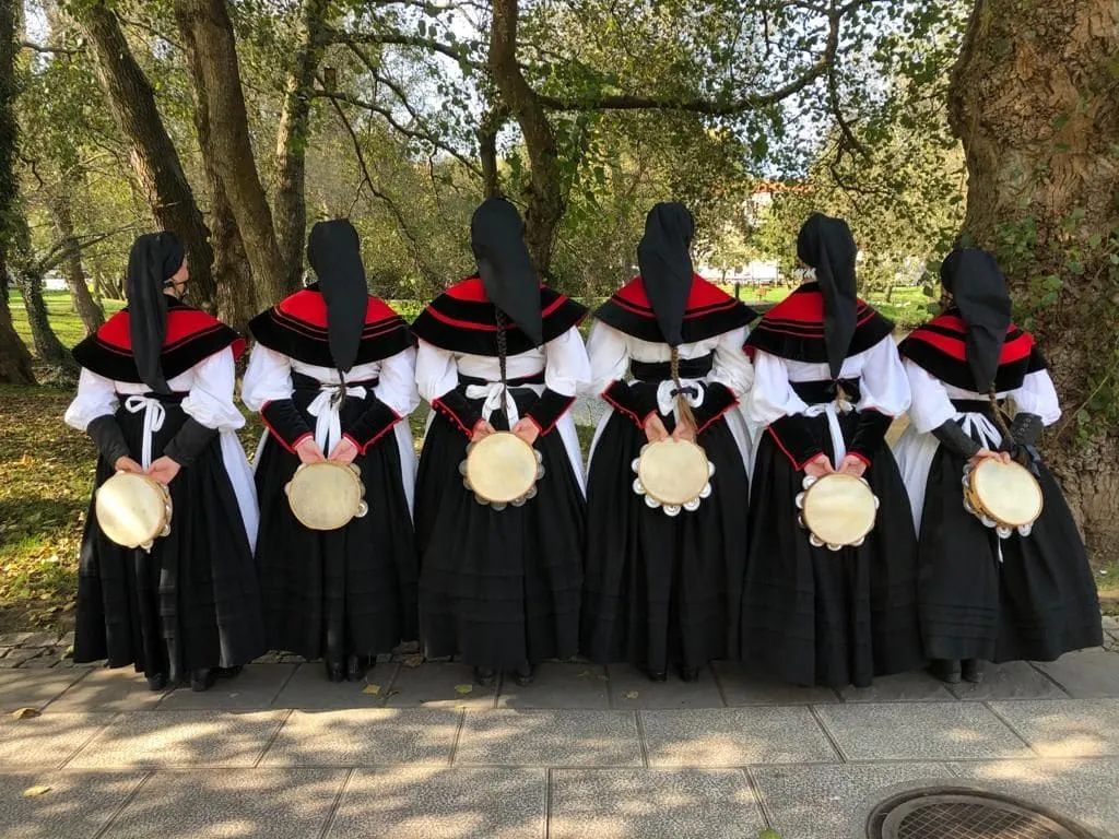 Cinco pandereteiras con traje tradicional gallego y panderetas en las manos, en un parque
