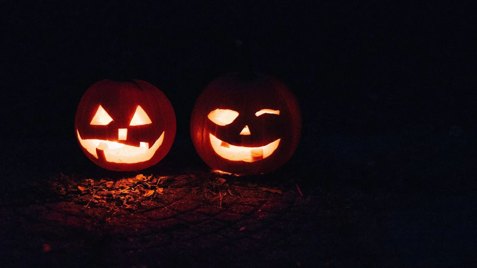 Dos calabazas talladas con cara, iluminadas desde dentro en la oscuridad