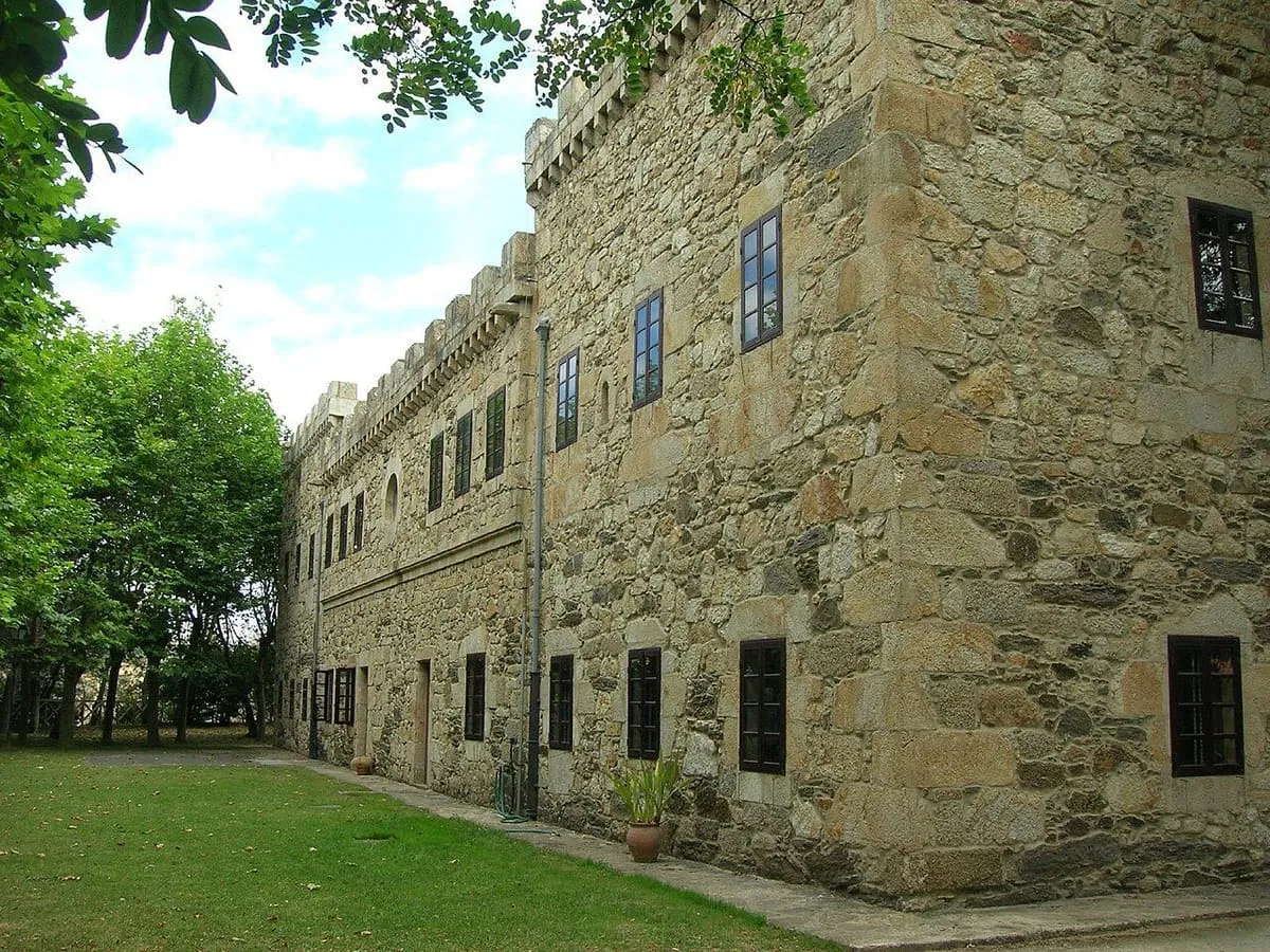Edificio de piedra con almenas rodeado de césped y árboles