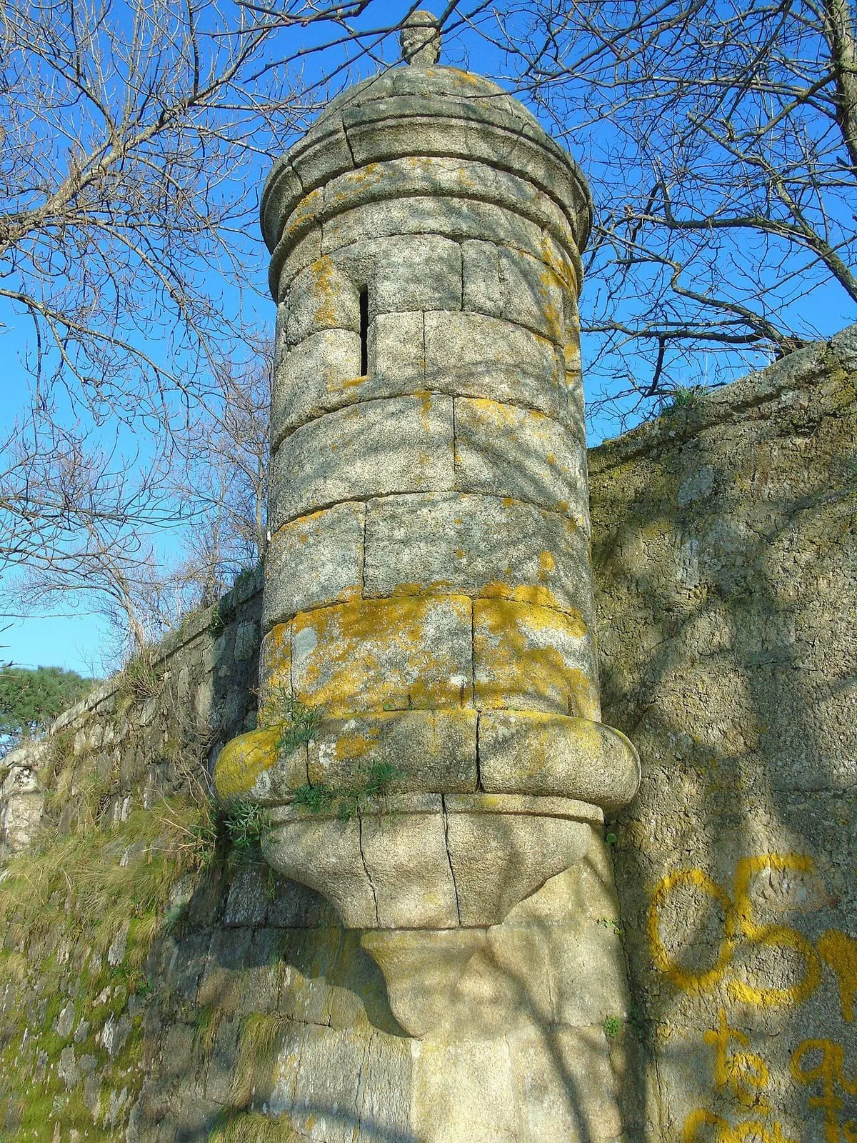 Garita cilíndrica de piedra en una esquina de la muralla, entre ramas desnudas