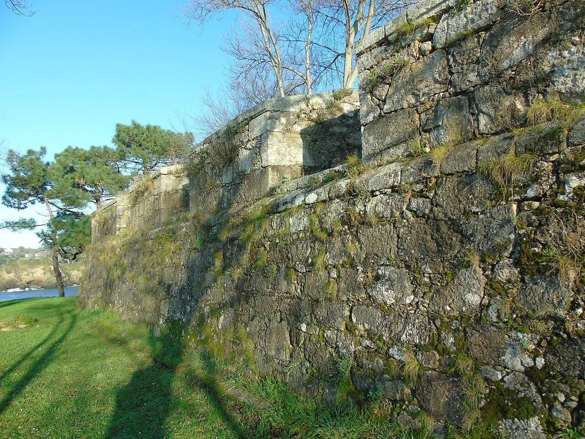 Muralla de piedra cubierta de líquenes sobre la hierba, junto al mar