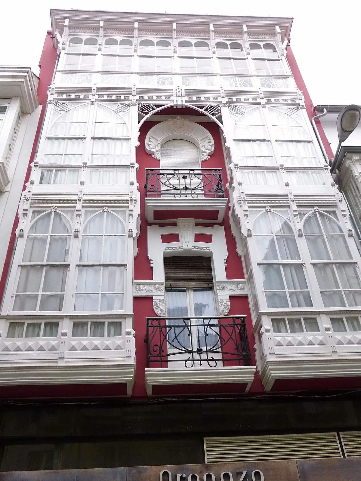 Fachada estrecha con galerías acristaladas blancas y detalles modernistas en rojo y blanco