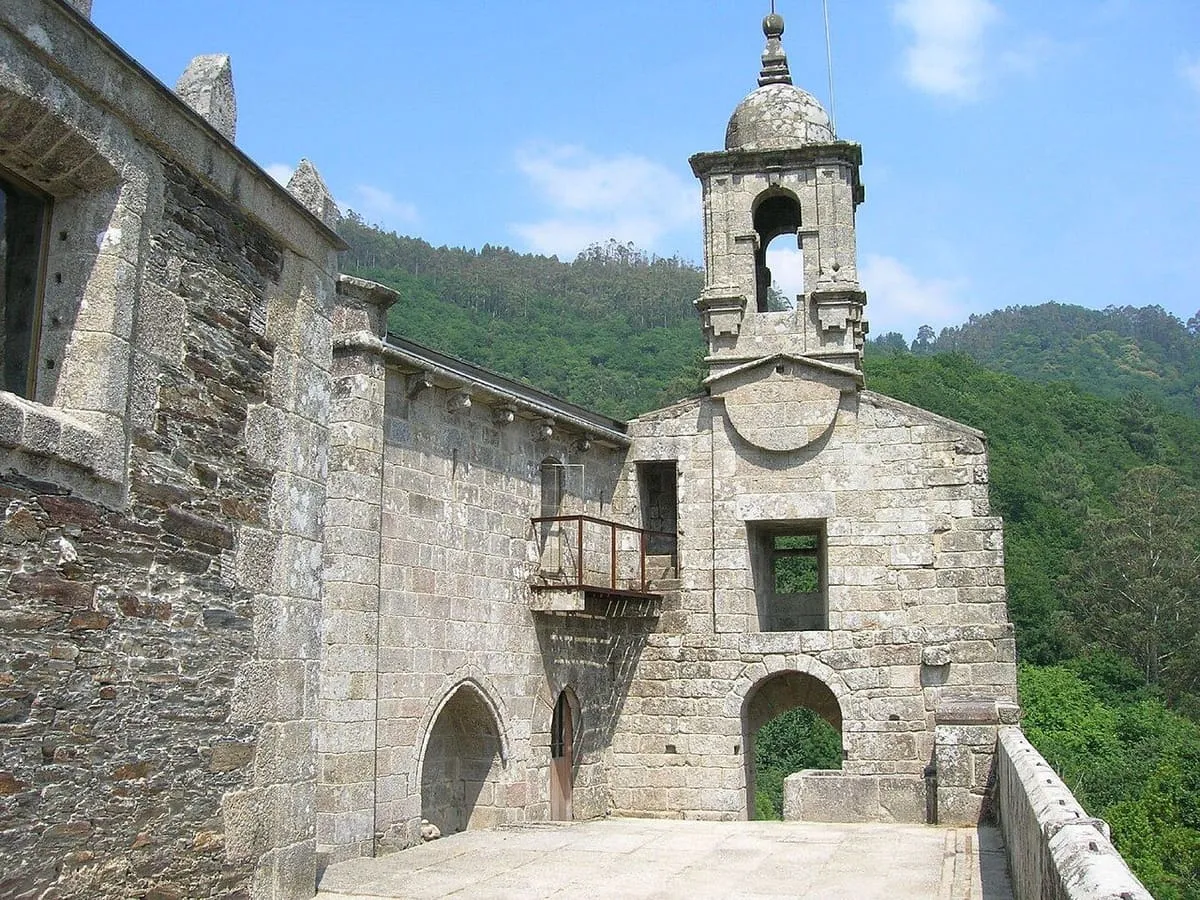 Muros de piedra y espadaña del monasterio con el bosque al fondo