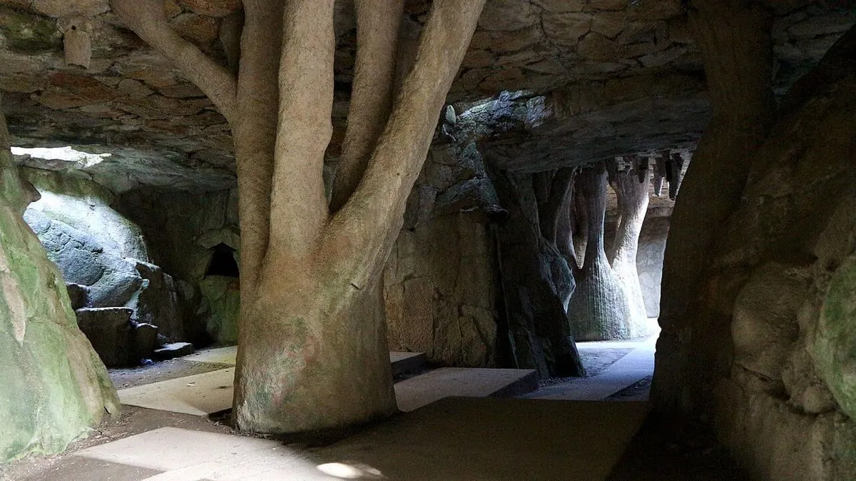 Interior de una gruta artificial con un tronco de piedra y luz que entra por las aberturas