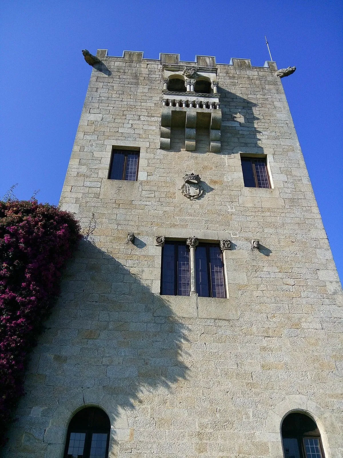 Torre almenada de piedra del pazo, con un balcón sobre la fachada y buganvilla a un lado