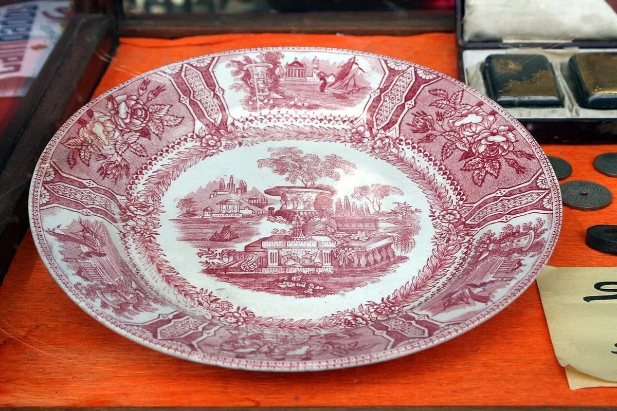 Plato de loza del siglo XIX decorado en rosa con un paisaje y orla de flores