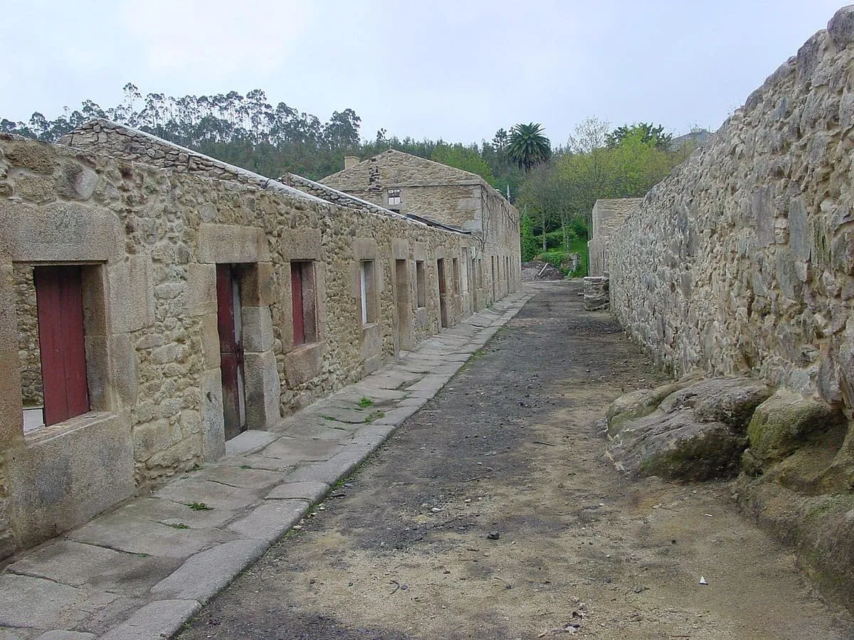 Calle de casas bajas de piedra con puertas y ventanas rojas junto a un muro