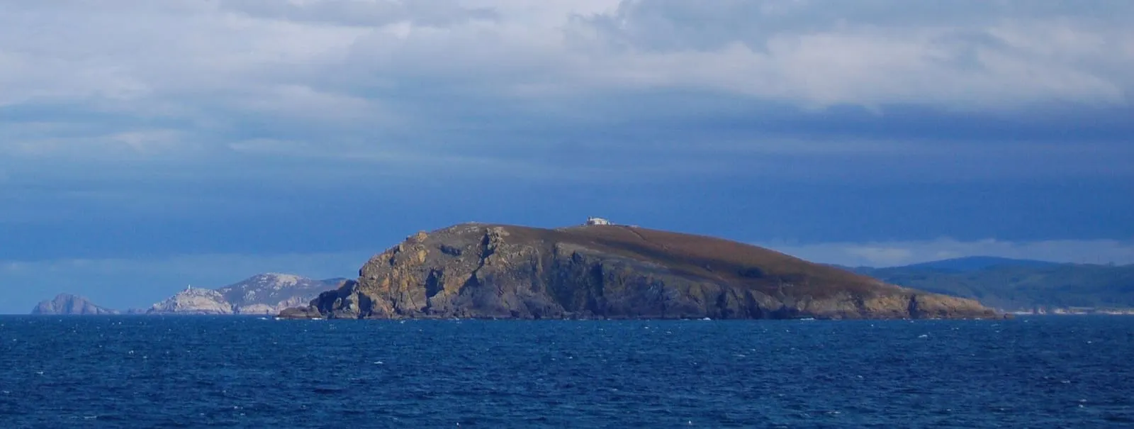 La isla Coelleira, con un faro en lo alto, recortada contra el mar y el cielo nuboso
