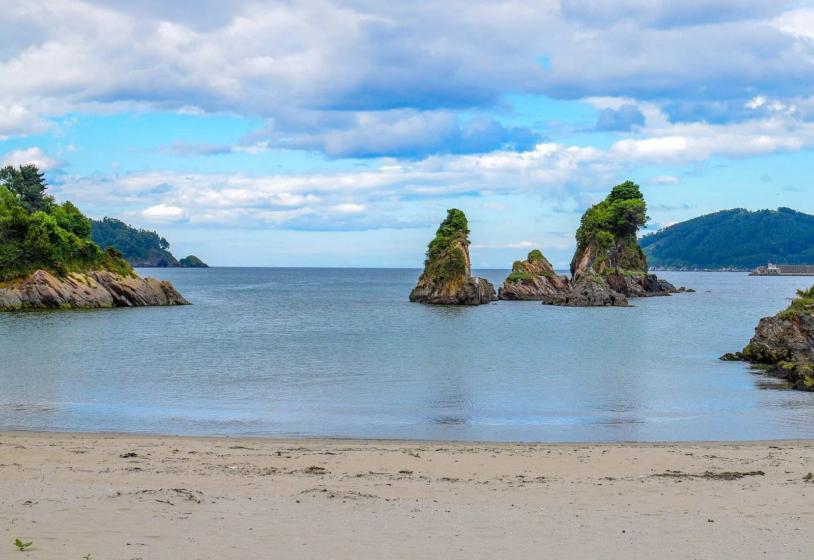 La playa de Covas, en Viveiro, con rocas en el agua y la costa al fondo